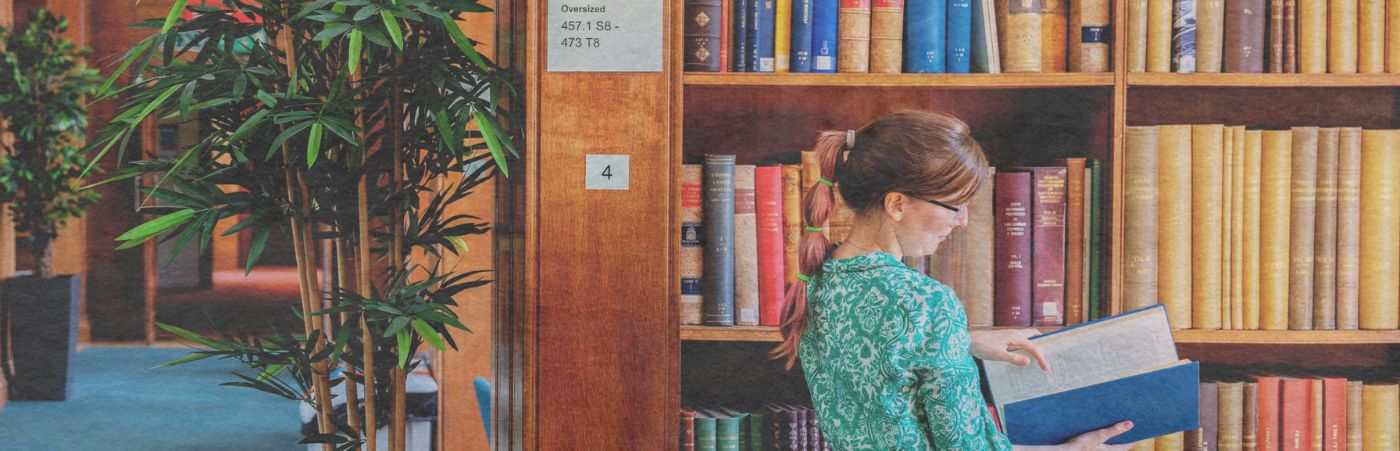 Woman looking at a book taken off a shelf in Main Library