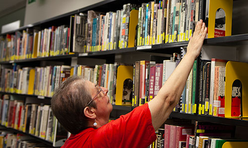 Photo: Woman reaching for book on a shelf in the library