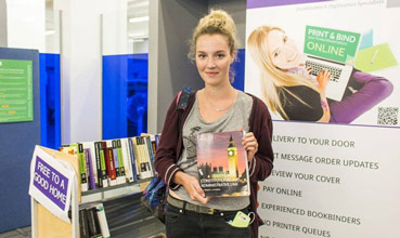 Student poses with a textbook at a previous textbook rescue event at Main Library