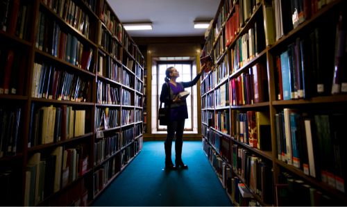 Woman reaching for a book on shelf