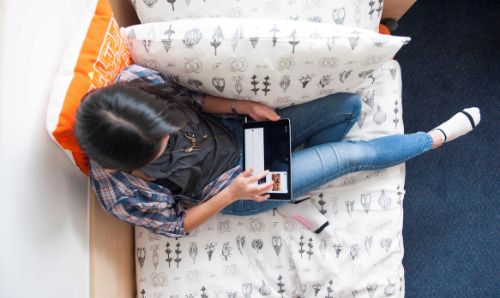 Woman sitting on bed looking at website on tablet device