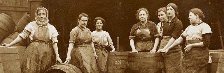 Seven working class women posing with wooden barrels in sepia photograph from the collection