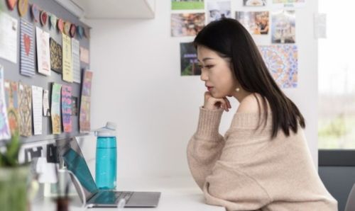 Student sitting at a desk with laptop in a bedroom in a University residence