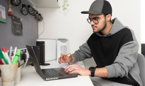 Student sitting at a desk working on a laptop in a bedroom in university accommodation