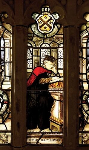Stained glass window of Richard Copley Christie, shown as a scholar, wearing academic gown and mortar-board.