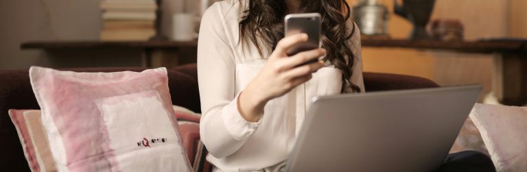 A woman looking at her phone with a laptop placed in her lap