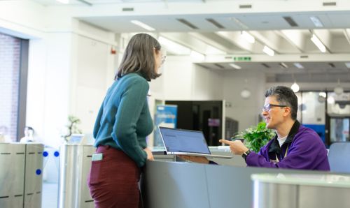 A member of Library staff at the reception in Main Library helping a customer