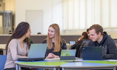 Students sat with laptops smiling in the Library Living Room