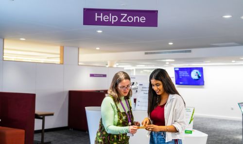 Library staff member assisting a student in Eddie Davies Library under a sign that reads Help Zone